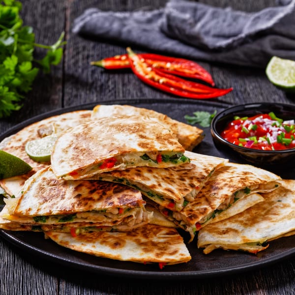 A plate of Chip Shots Pub's quesadillas with salsa, lime, and chili peppers on a dark wooden table.