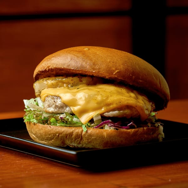 A Chip Shots Pub burger with melted cheese, grilled pineapple, lettuce, and red onion on a bun.